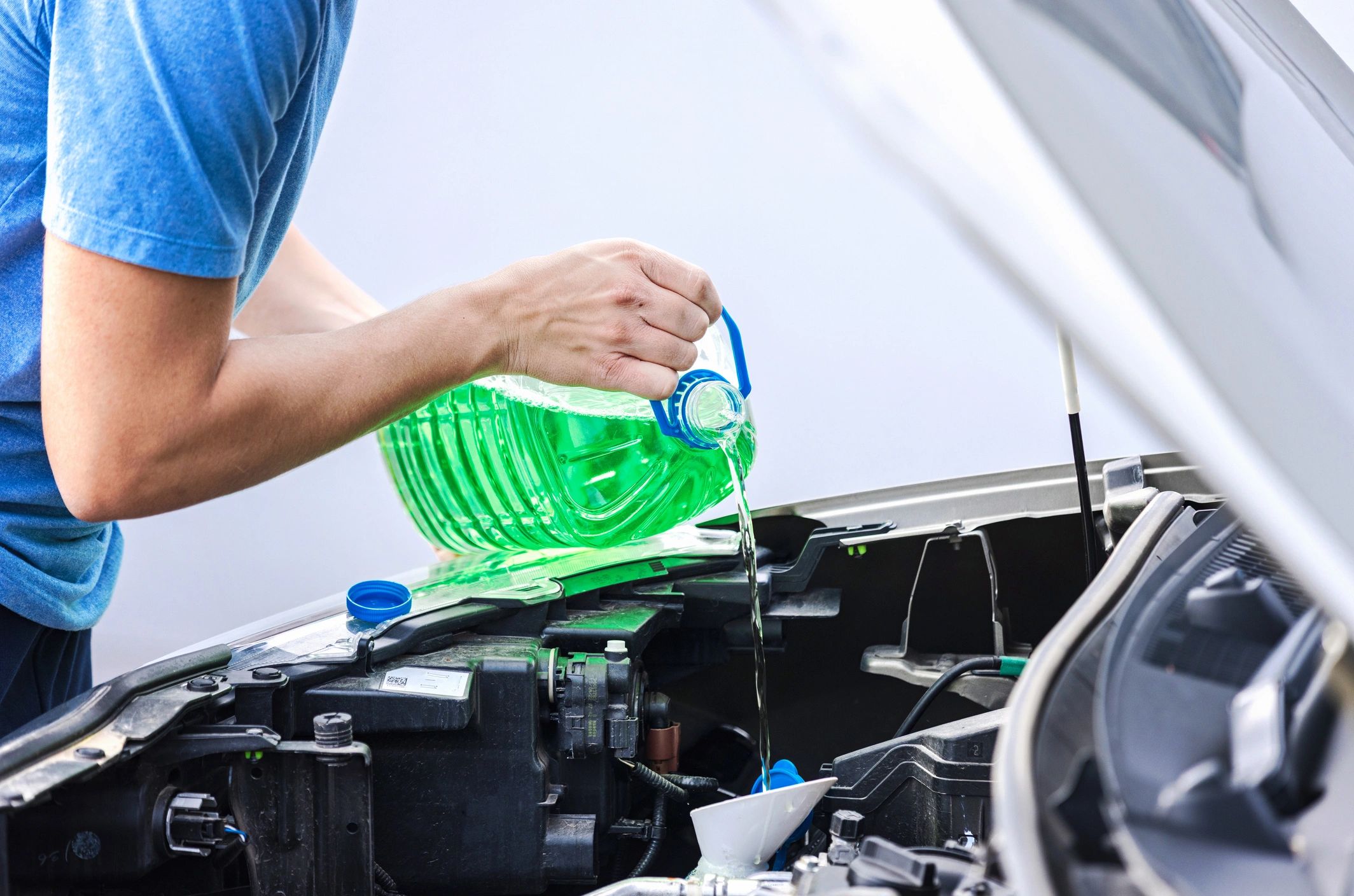 Technician adding automotive fluid under a vehicle hood